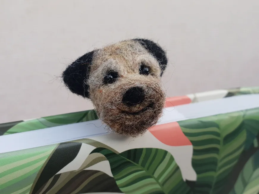A felted Border Terrier face bookmark peeping over the top of a book
