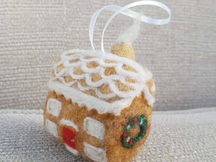 A needle-felted gingerbread house decoration with a ribbon loop