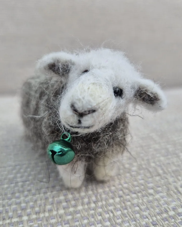 A needle-felted Herdwick sheep with a green bell on its collar